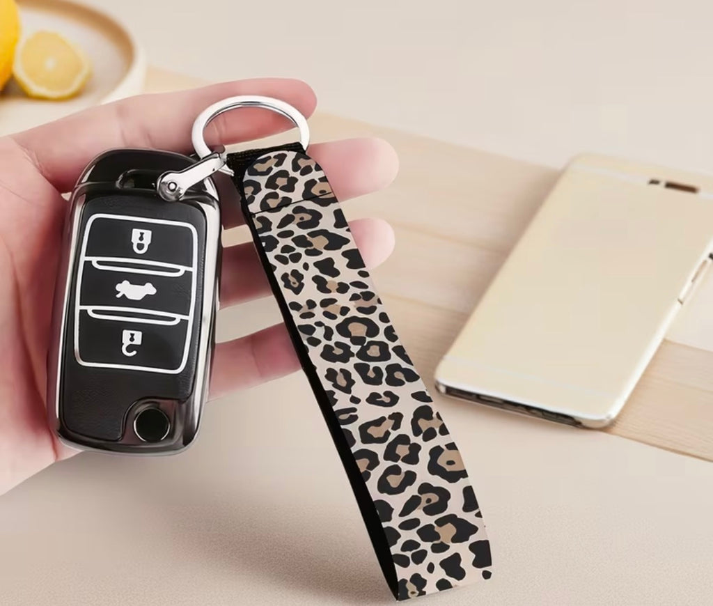 Car key fob with leopard print keychain held by a hand on a light surface.