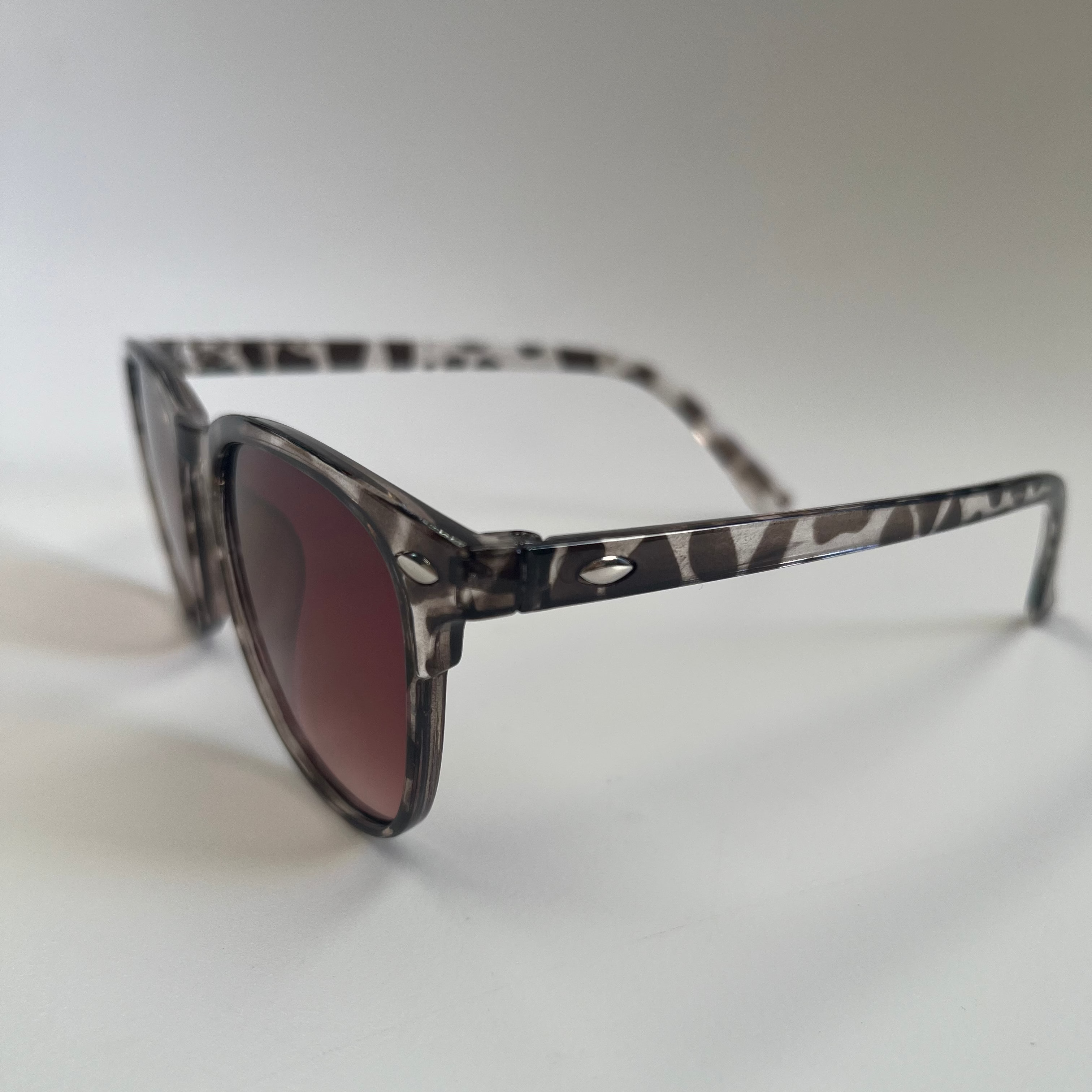 Sunglasses with a patterned frame and dark lenses on a light gray background