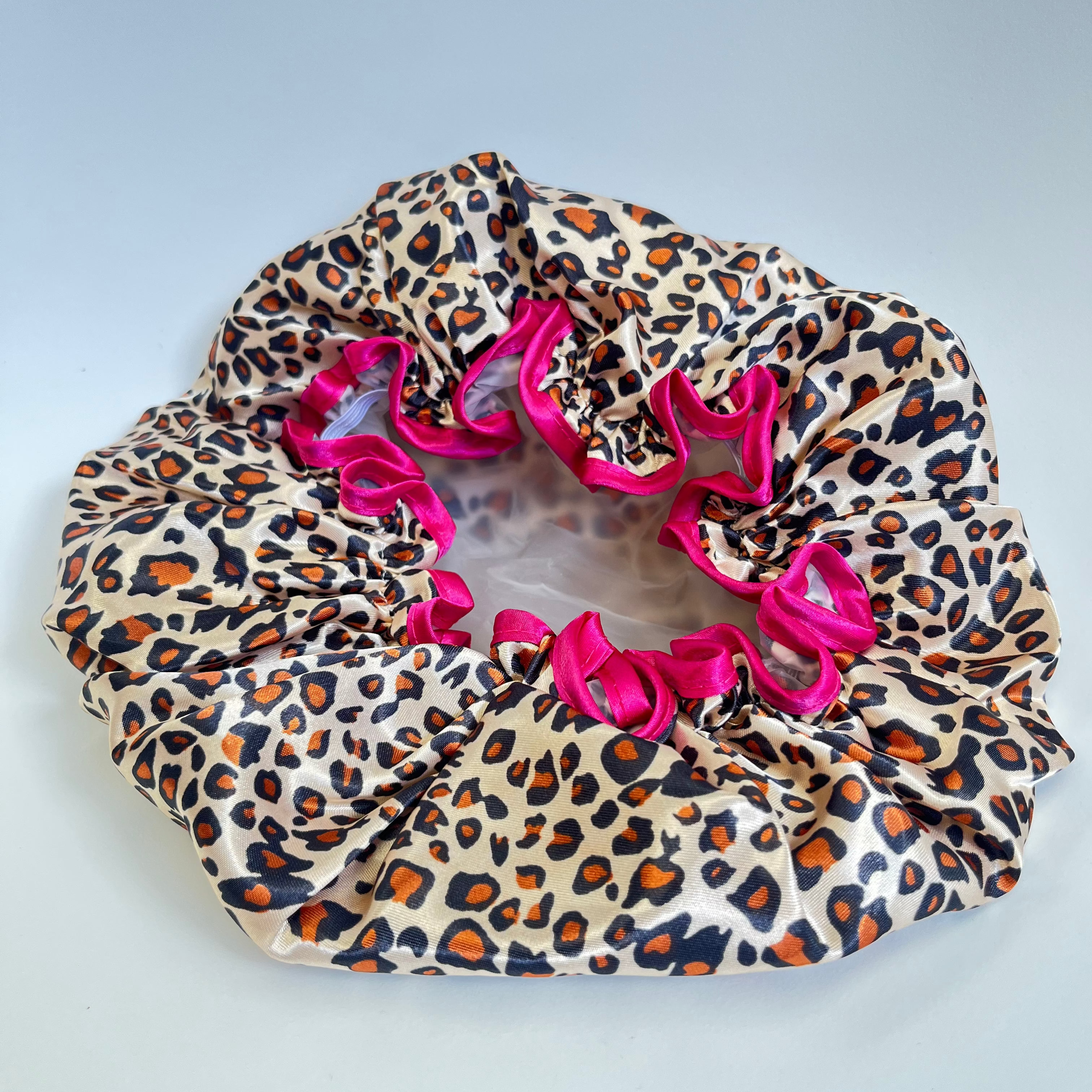 Leopard print hair bonnet with pink trim on a light gray background