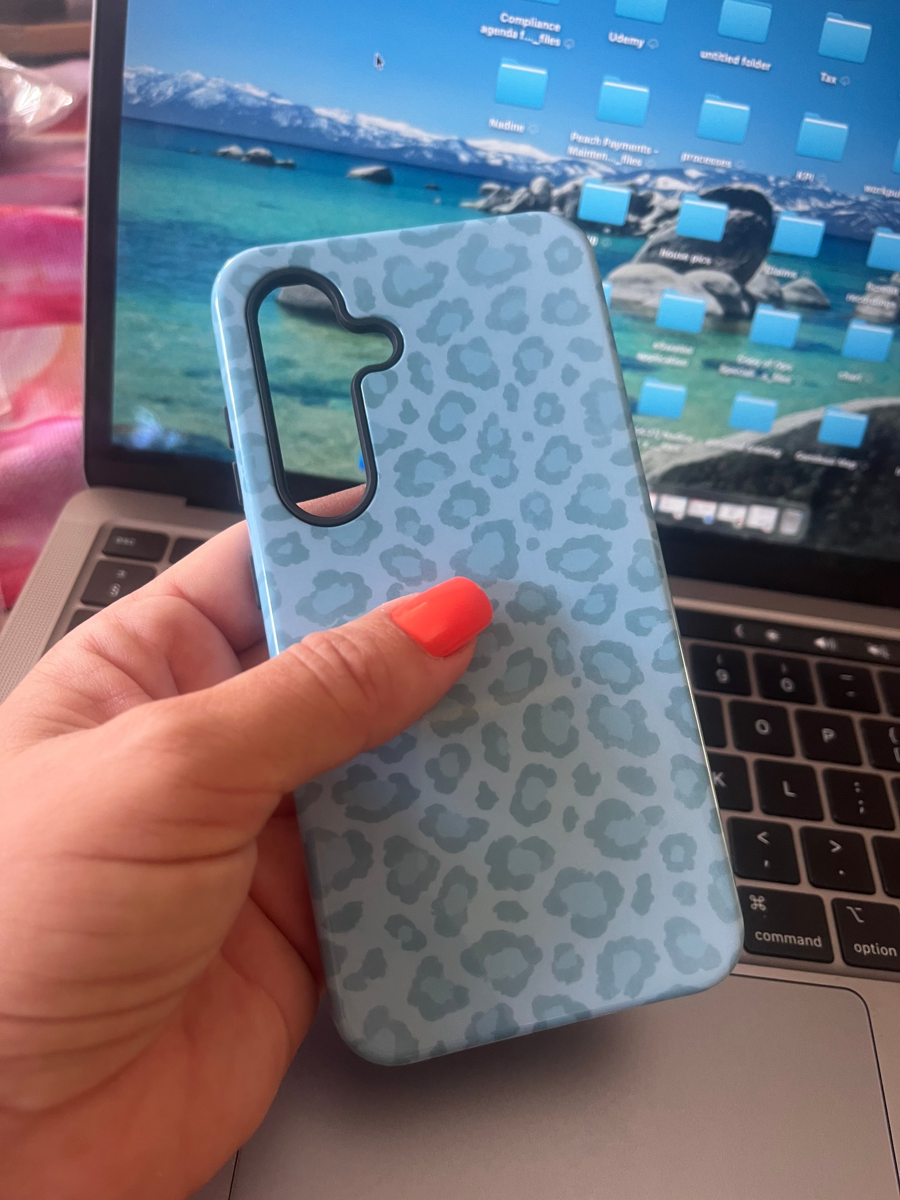 Hand holding a phone case with a leopard print pattern in front of a laptop.