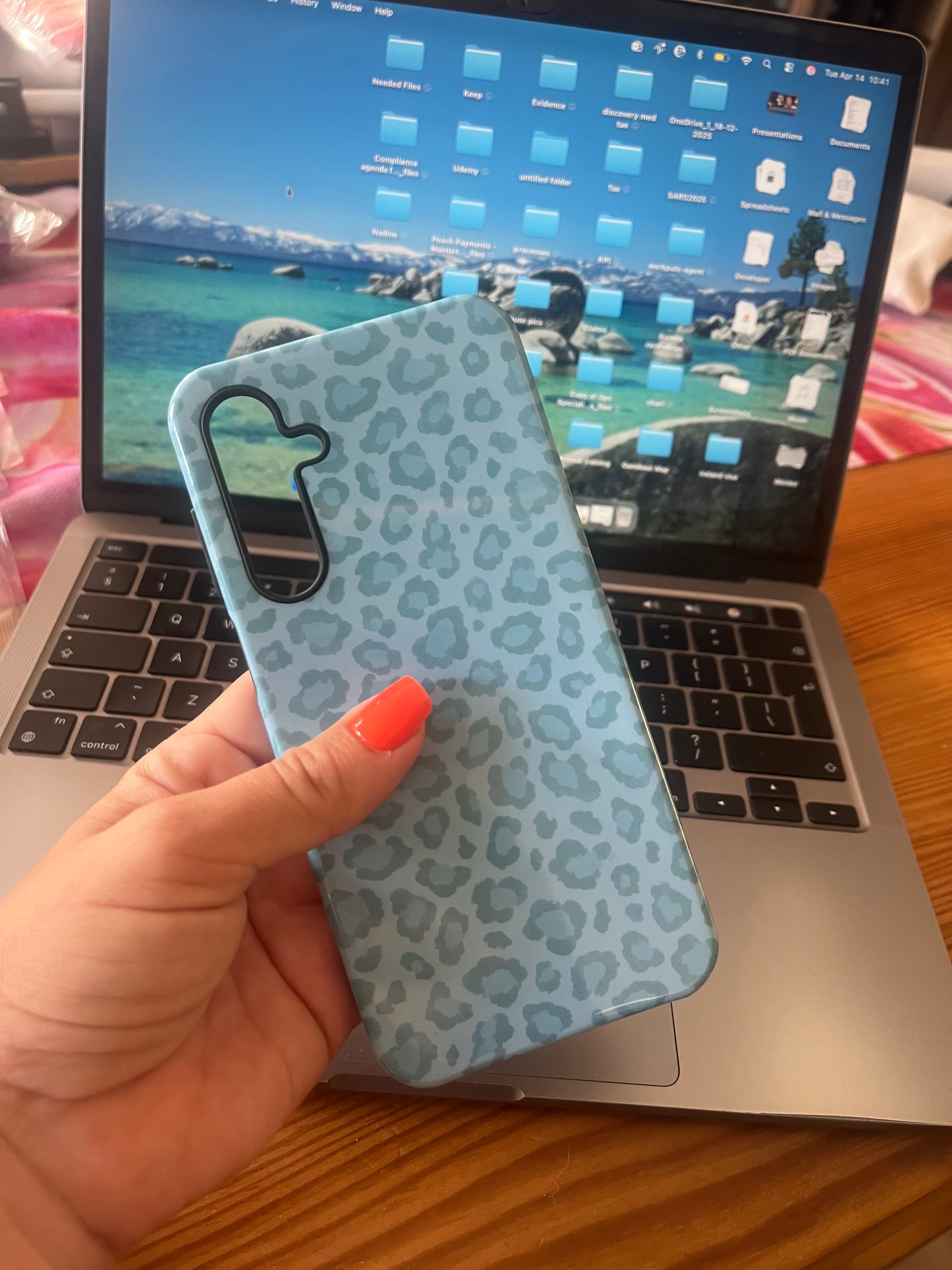Hand holding a blue leopard print phone case in front of an open laptop.