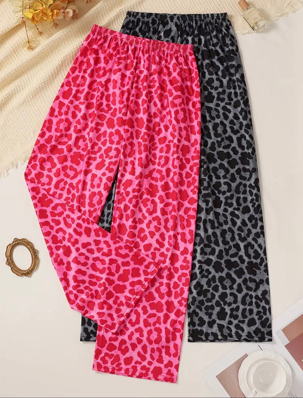 Two pairs of leopard print pants, one pink and one black, on a light background.