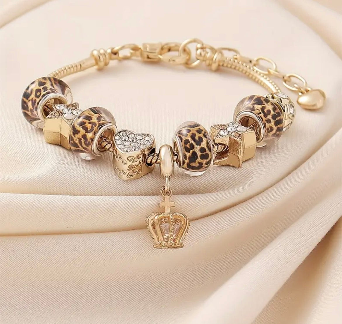 Gold bracelet with leopard print and heart charms on a beige fabric background