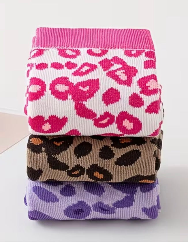 Stack of three patterned socks with pink leopard, brown leopard, and purple leopard designs on a white background.