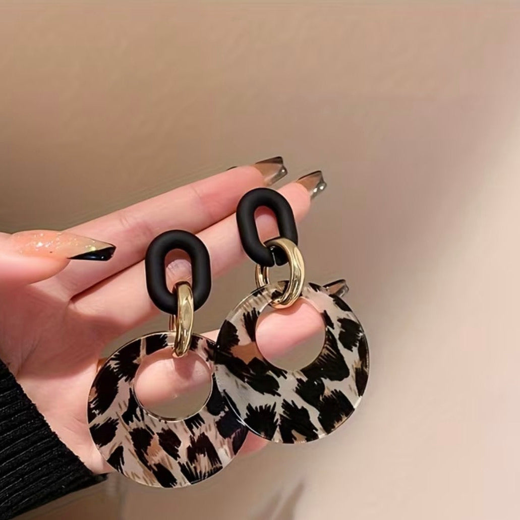 Leopard print earrings held by a hand against a beige background