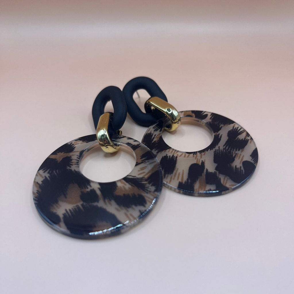 Leopard print earrings with navy blue rubber bands on a light pink background