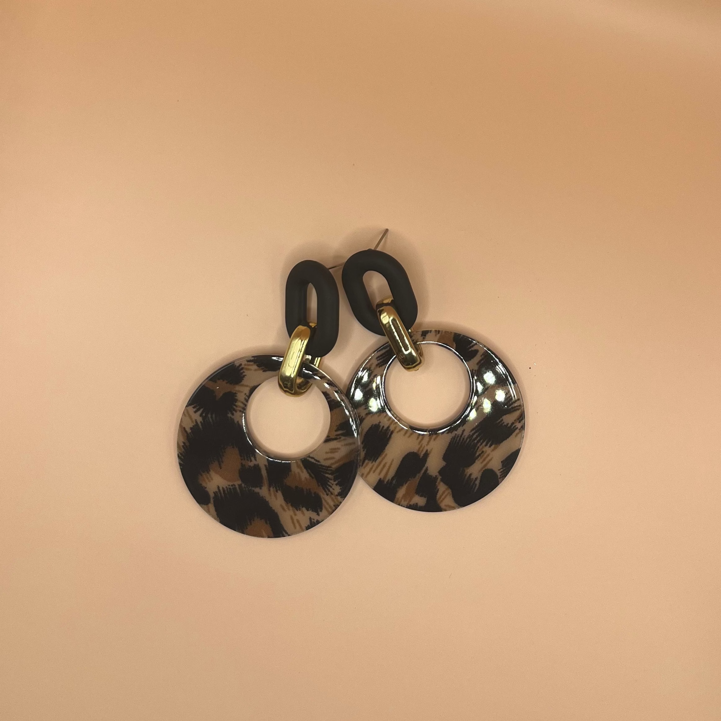 Pair of earrings with leopard print design on a beige surface.