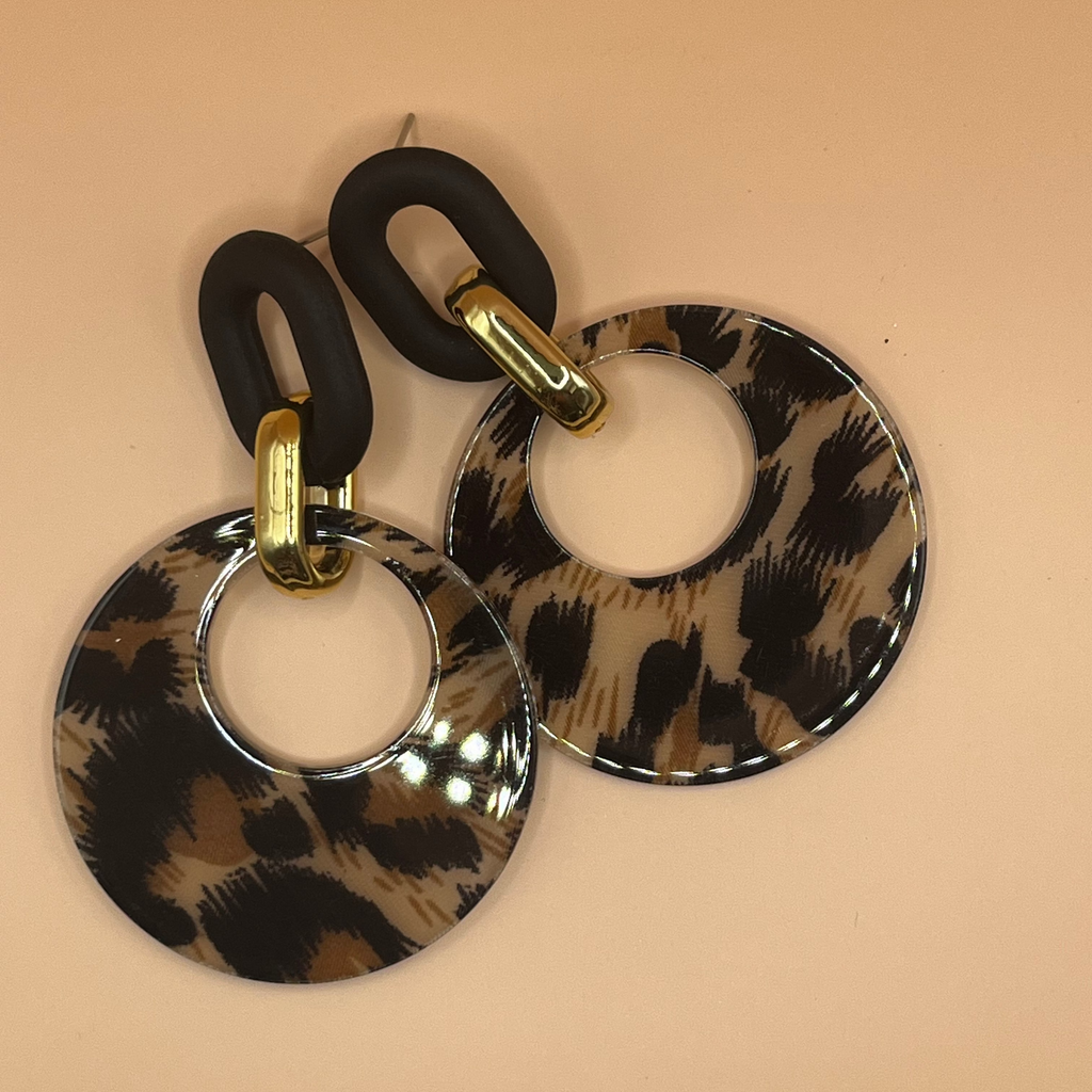 Pair of earrings with leopard print and gold accents on a beige background