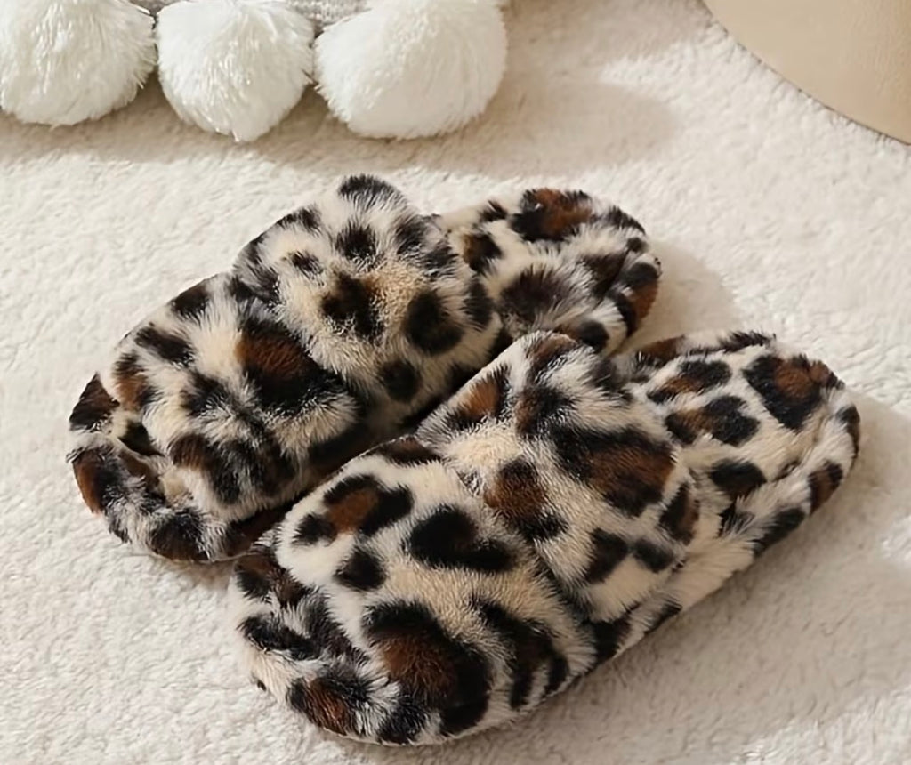 Leopard print slippers on a white surface with white pom-poms in the background