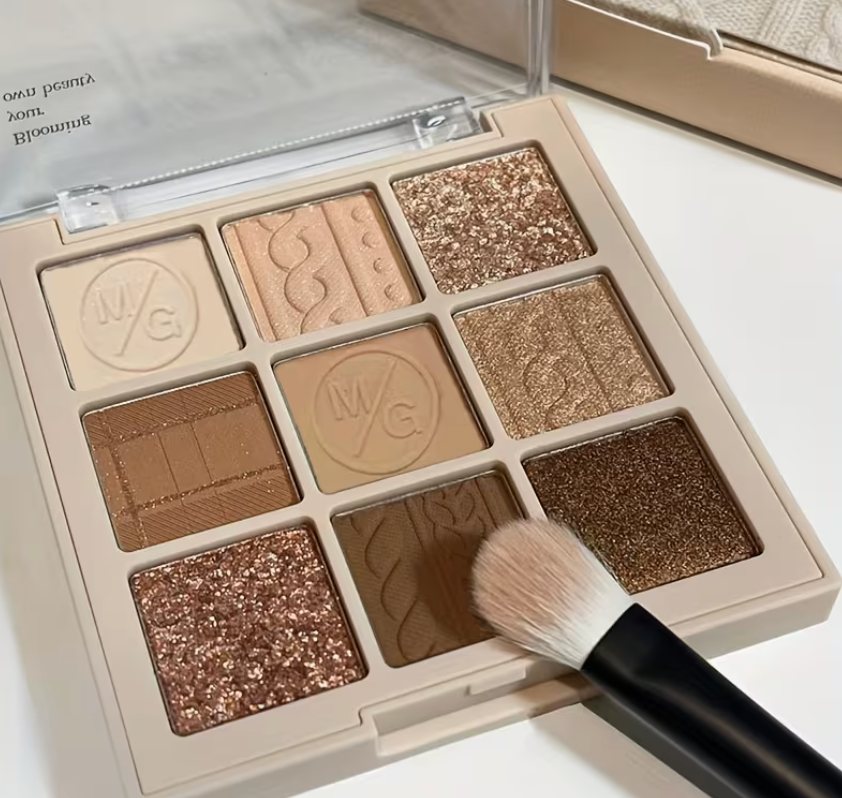 Makeup palette with brown and gold shades and a brush on a white background