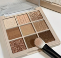 Makeup palette with brown and gold shades and a brush on a white background