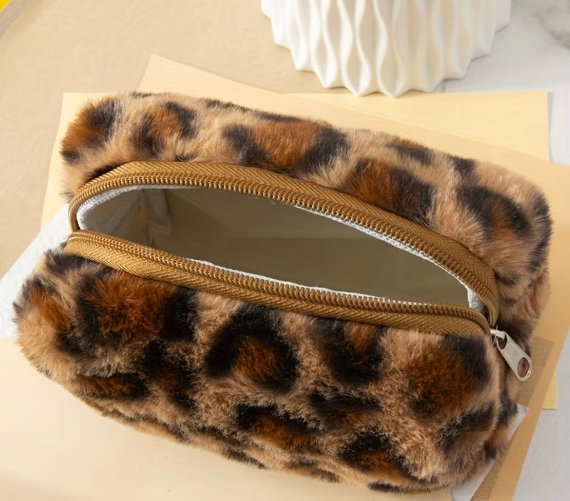 Leopard print clutch bag with a gold zipper on a beige surface
