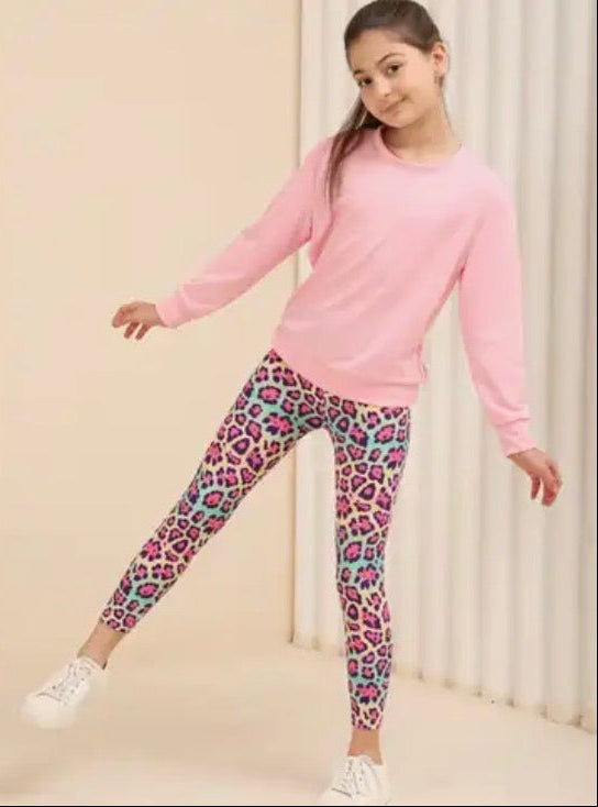 Girl wearing a pink sweatshirt and colorful leopard print leggings on a beige background