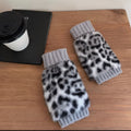 Leopard print arm warmers with light gray cuffs on a wooden surface next to a coffee cup and laptop.