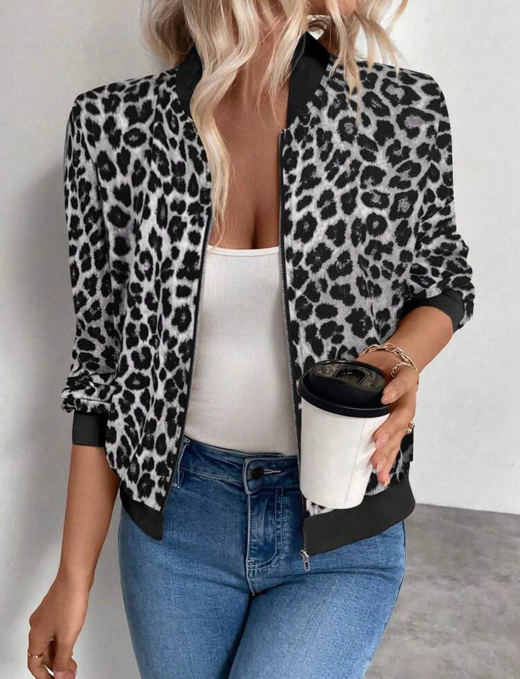 Person wearing a leopard print jacket, white top, and blue jeans holding a coffee cup.