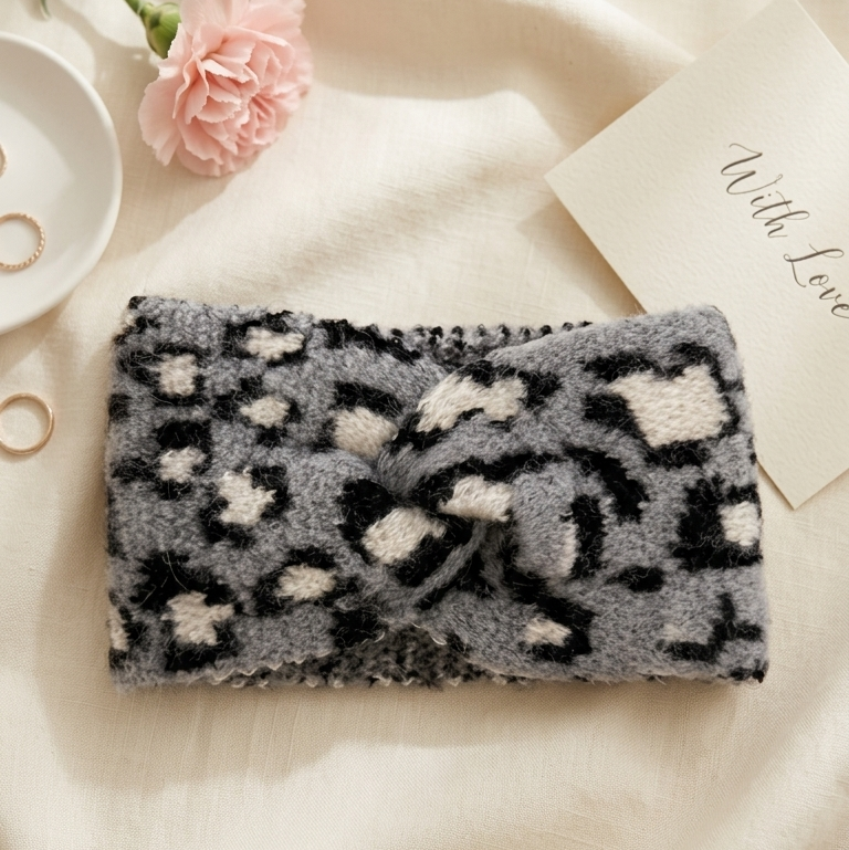 Fluffy black and white patterned pouch on a soft beige surface with a pink flower and white dish in the background.