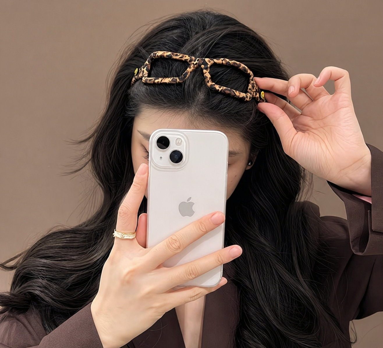 Person holding a phone with a leopard print hair accessory on a plain background