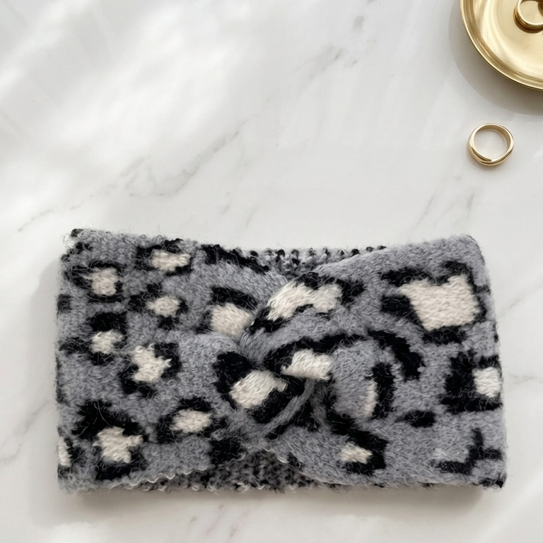 Gray leopard print headband on a marble surface with a gold ring and button in the background.