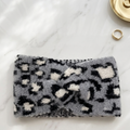 Gray leopard print headband on a marble surface with a gold ring and button in the background.