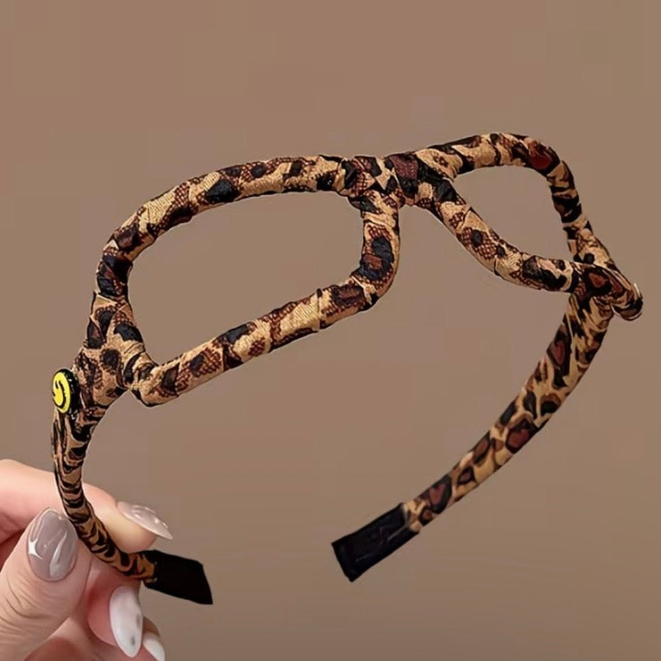 Leopard print headband held by a hand against a brown background