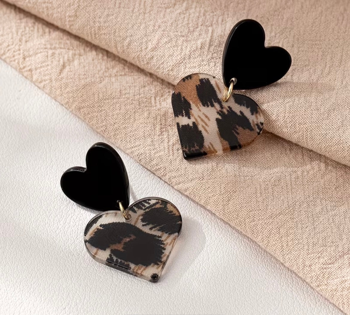 Heart-shaped earrings with leopard print design on a beige fabric background