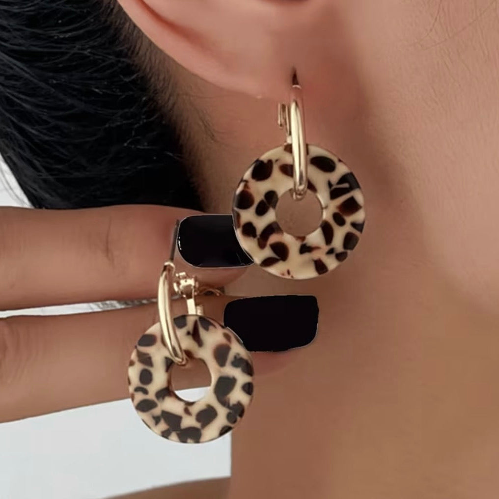 Leopard print earrings worn by a person against a neutral background