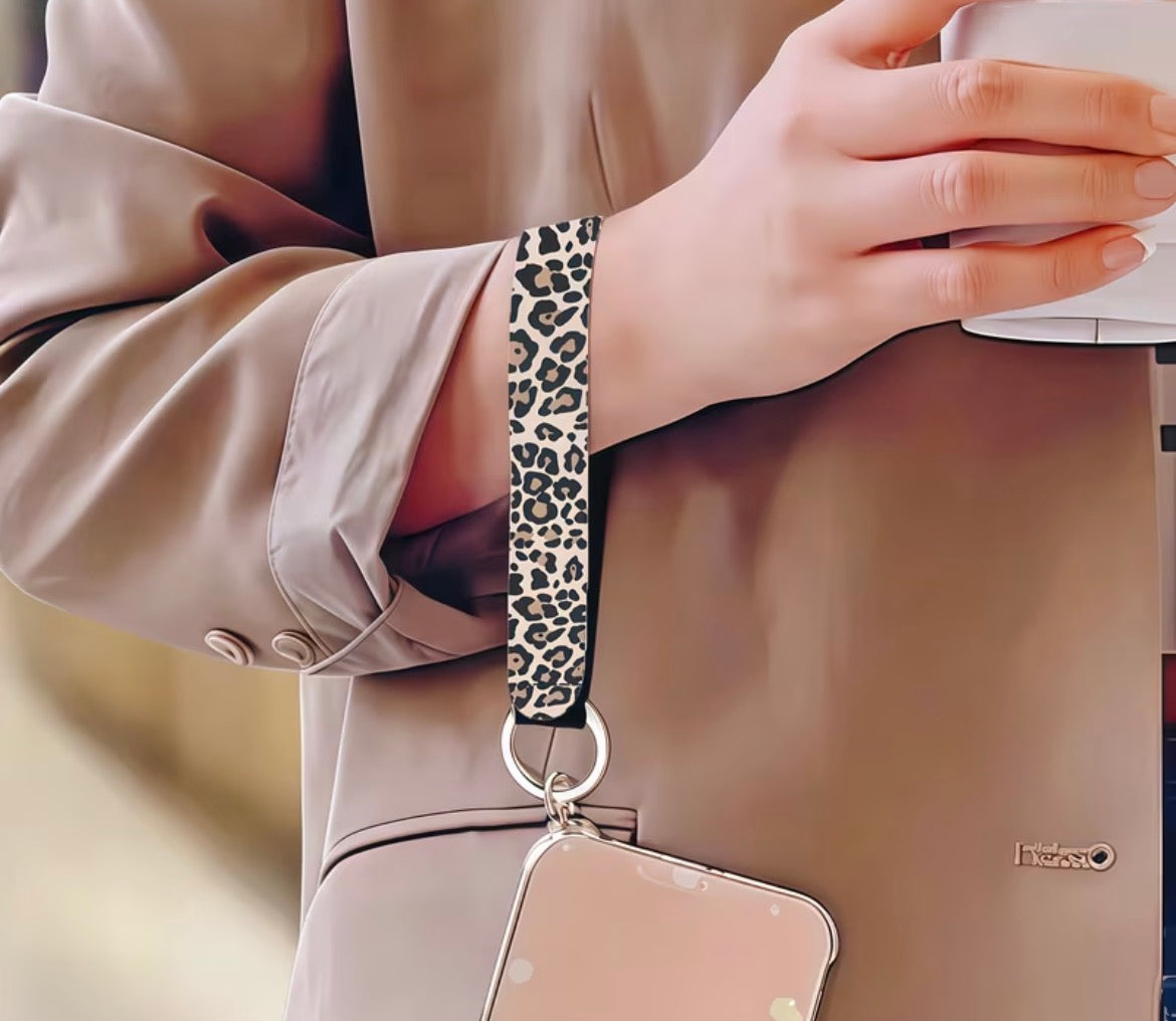 Person holding a phone case with a leopard print strap, wearing a beige coat.