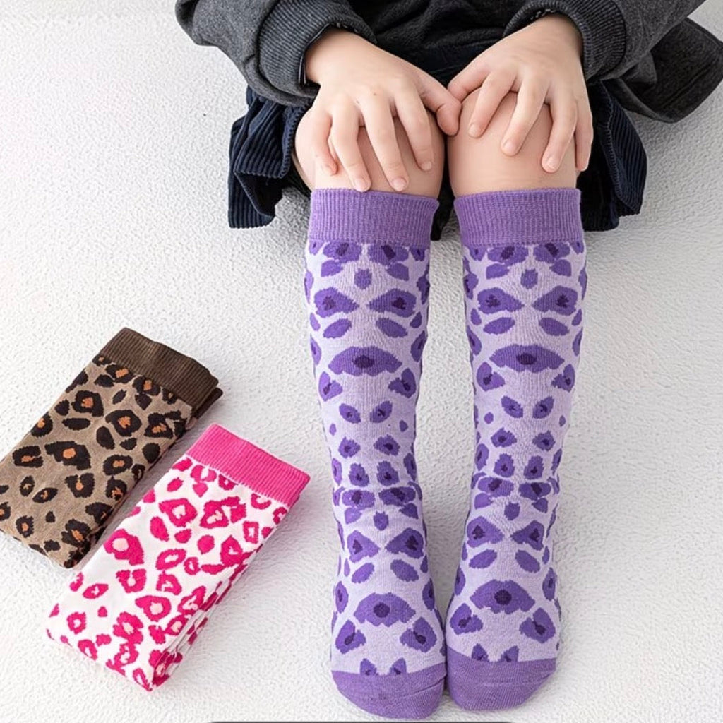 child wearing purple leopard print socks with two additional pairs of socks displayed in front.