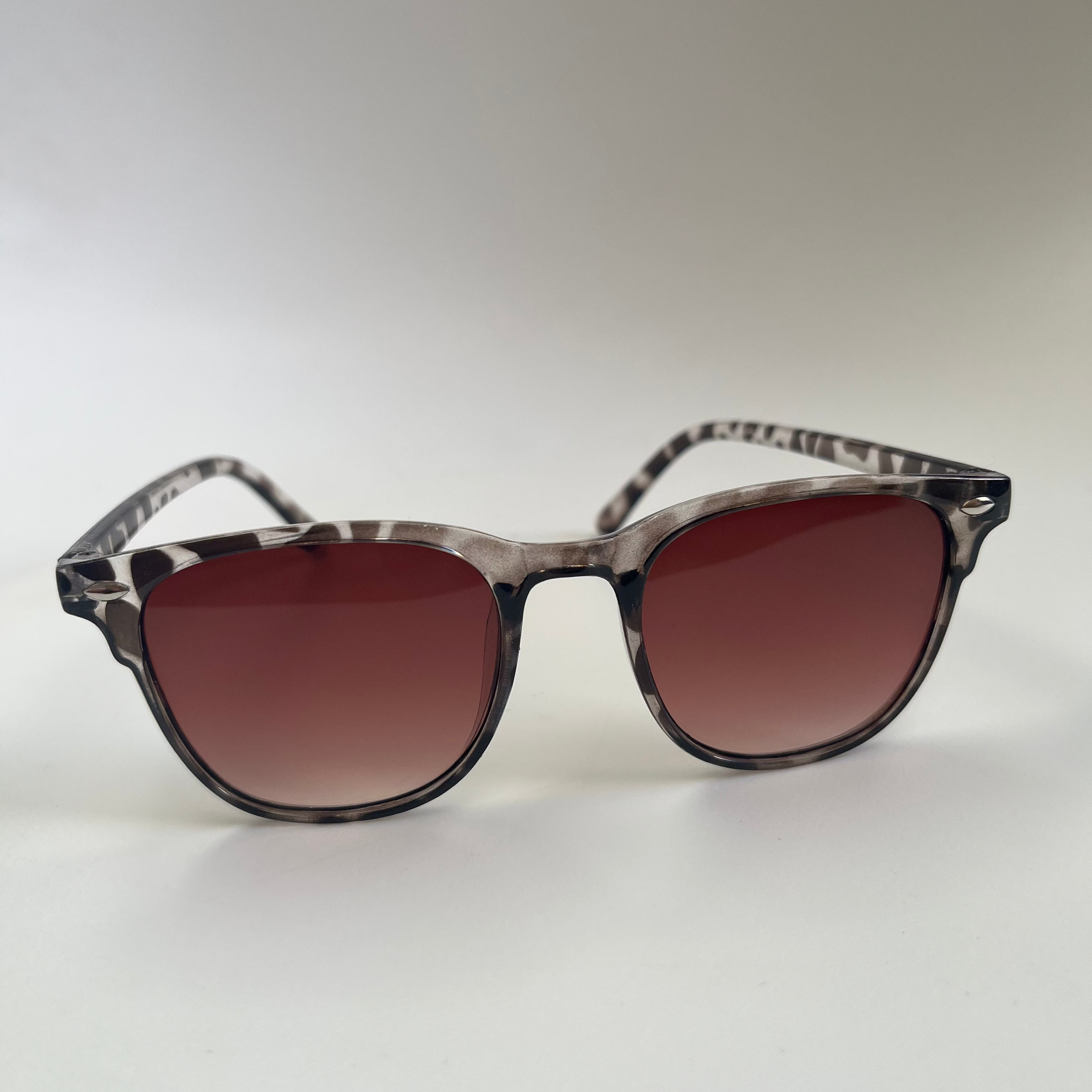 Sunglasses with a leopard print frame and brown lenses on a light gray background