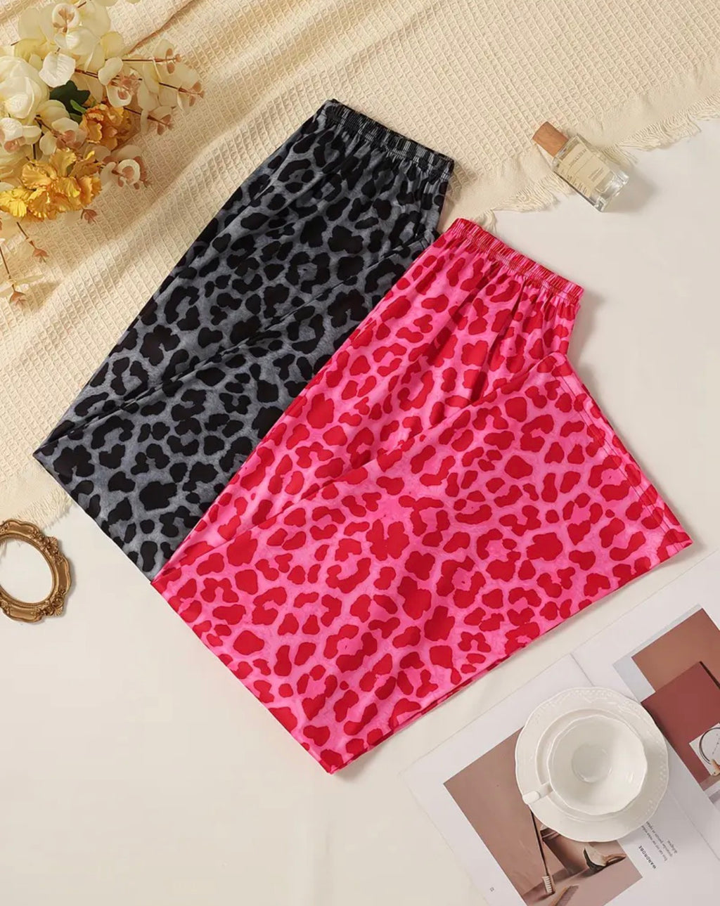 Two leopard print pants, one black and one pink, on a light surface with decorative items.
