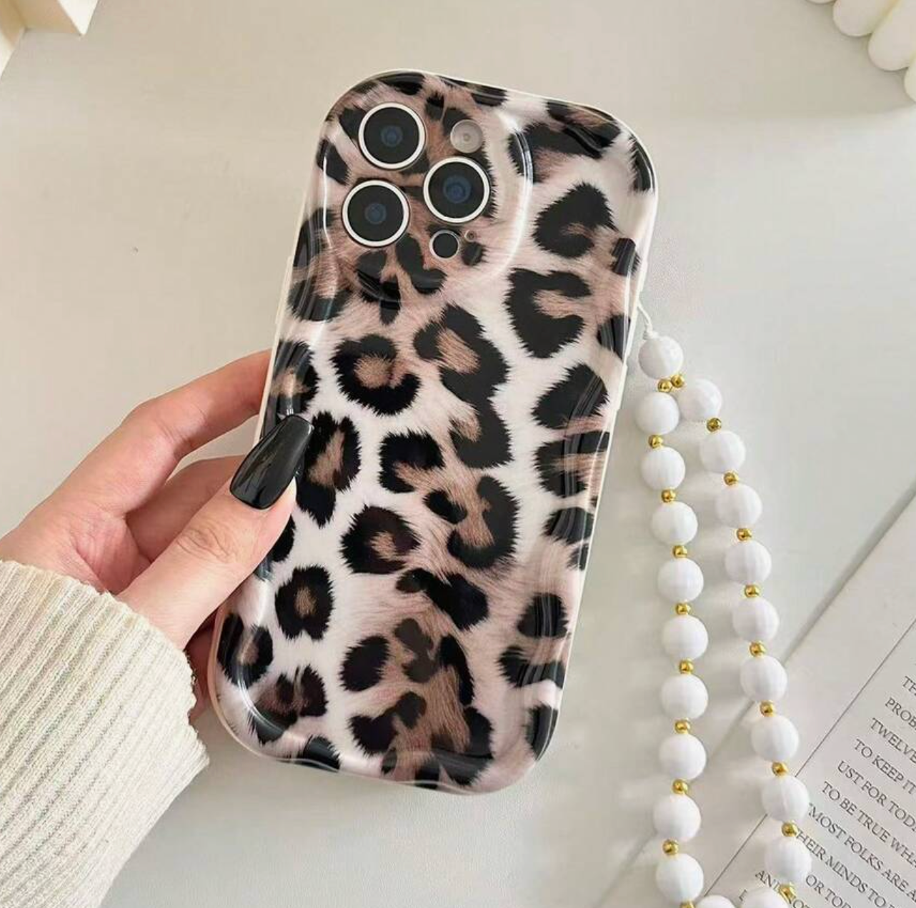 Phone case with leopard print held by a hand on a light surface.