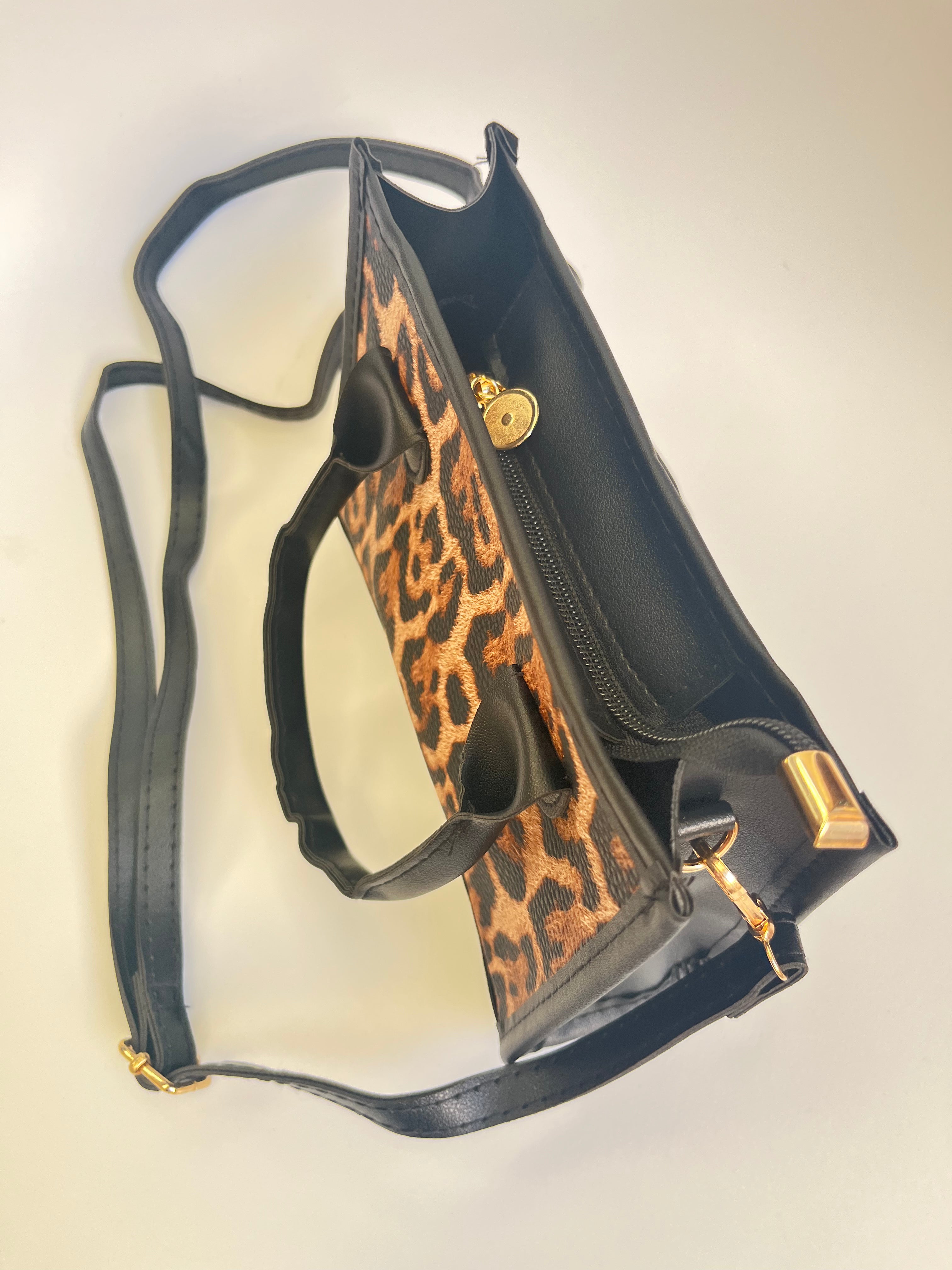 Black handbag with leopard print accents on a light beige background