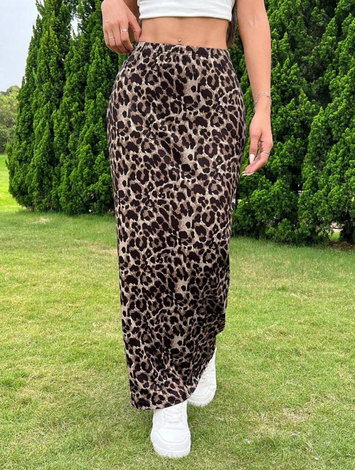 Person wearing a leopard print skirt outdoors on a grassy area with trees in the background