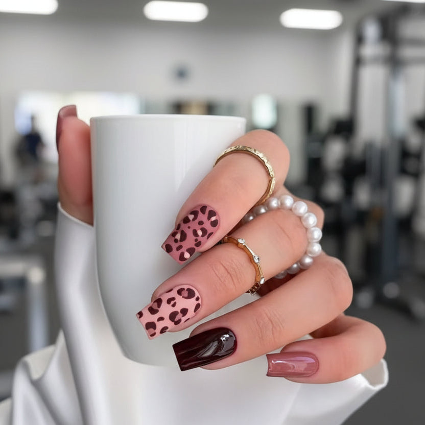Hand with leopard print nails holding a white mug in an indoor setting