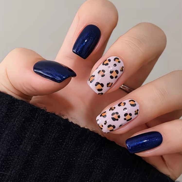 Hand with navy and leopard print nails against a neutral background