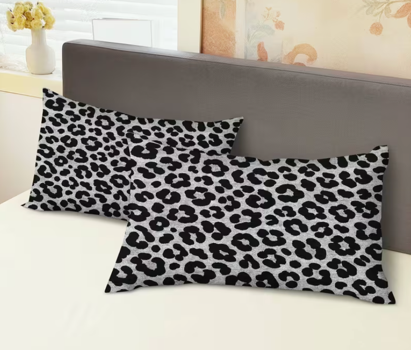 Two leopard print pillows on a bed with a neutral headboard.