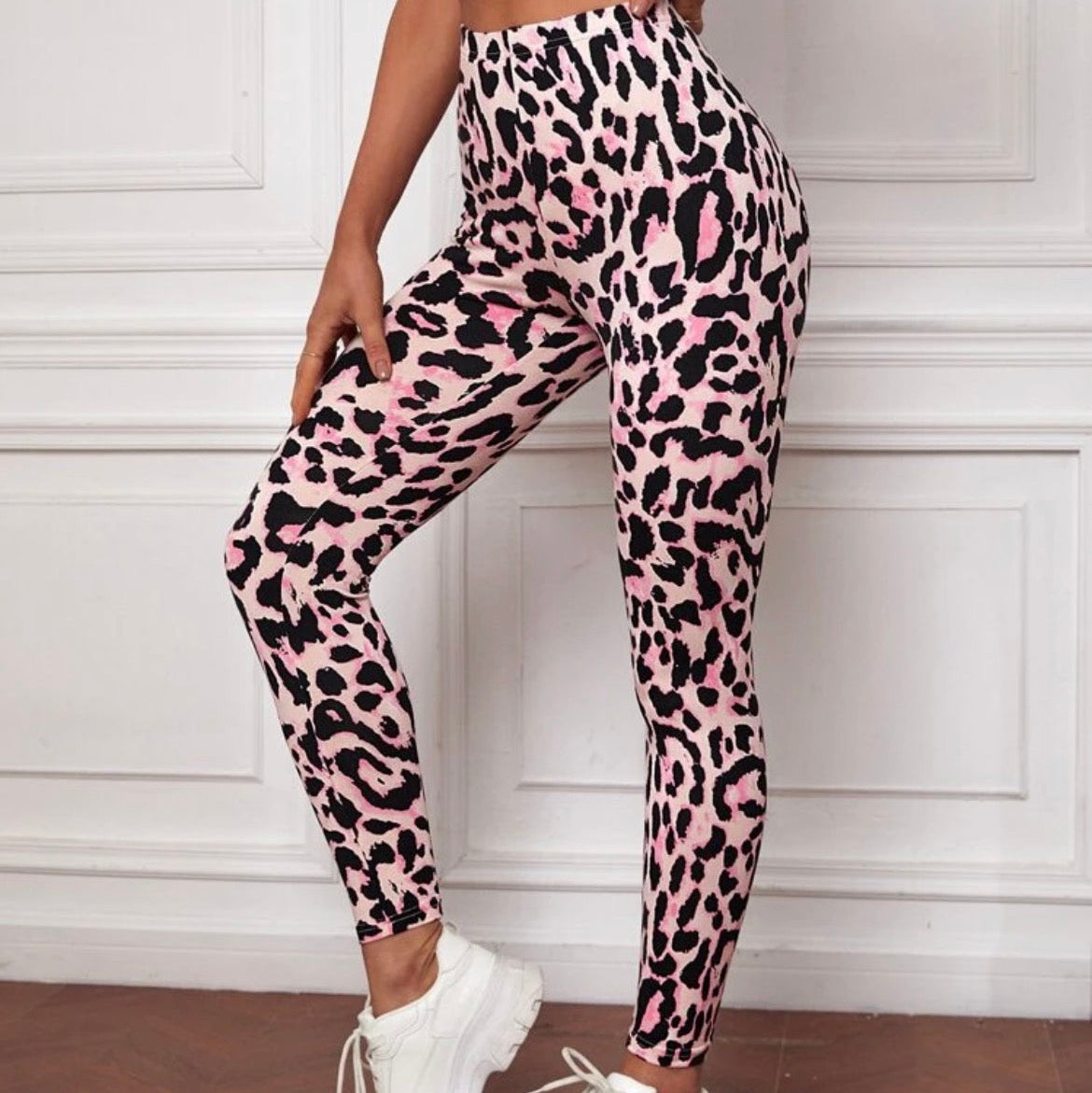 Person wearing pink leopard print leggings with white sneakers in a room with white paneled walls.