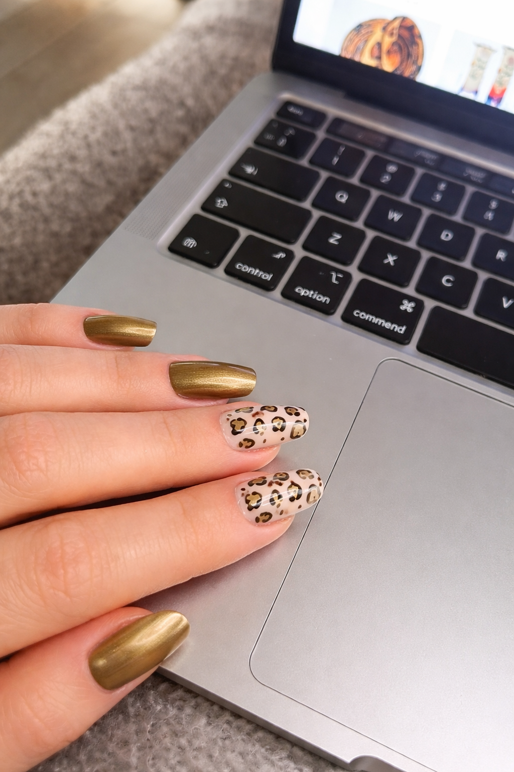 Hand with gold and leopard print nails on a laptop keyboard