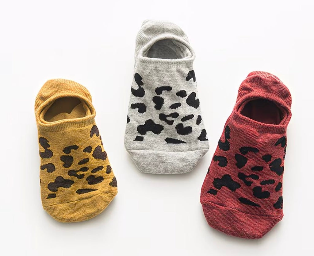 Three pairs of leopard print socks in yellow, gray, and red on a white background