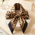 Leopard print scarf tied in bow on a white box with a card and flowers in the background
