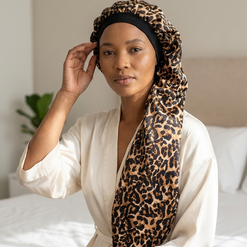 Woman wearing a leopard print sleep cap and white robe on a bed.