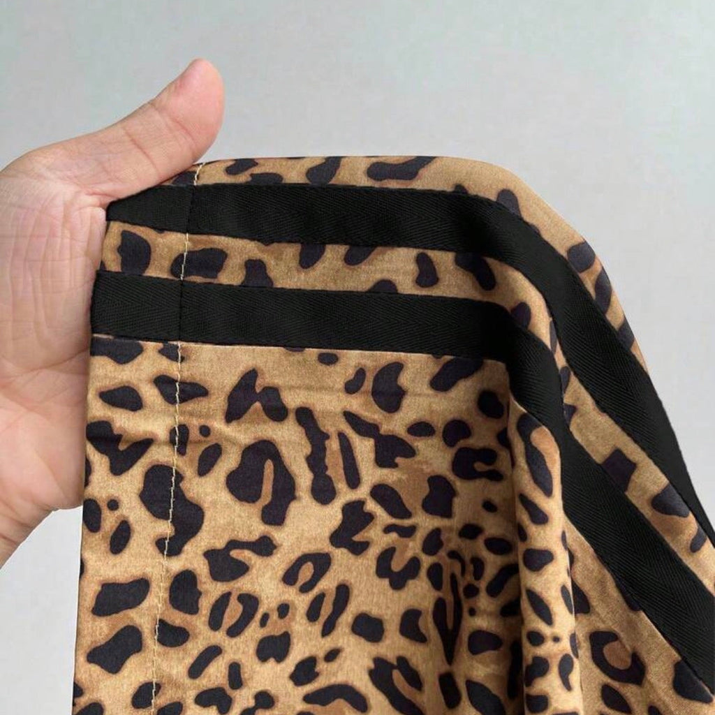 Leopard print fabric with a black border held by a hand against a gray background
