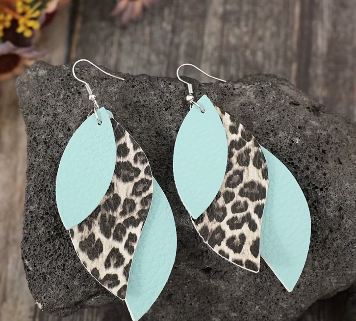 Leopard print and light blue leaf-shaped earrings on a textured stone surface.