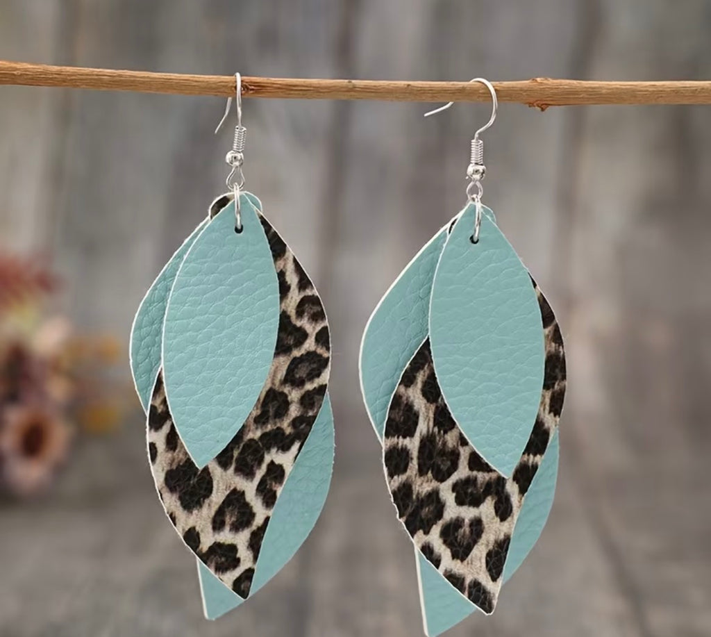 Leopard print and light blue leaf-shaped earrings hanging on a branch with a blurred natural background.